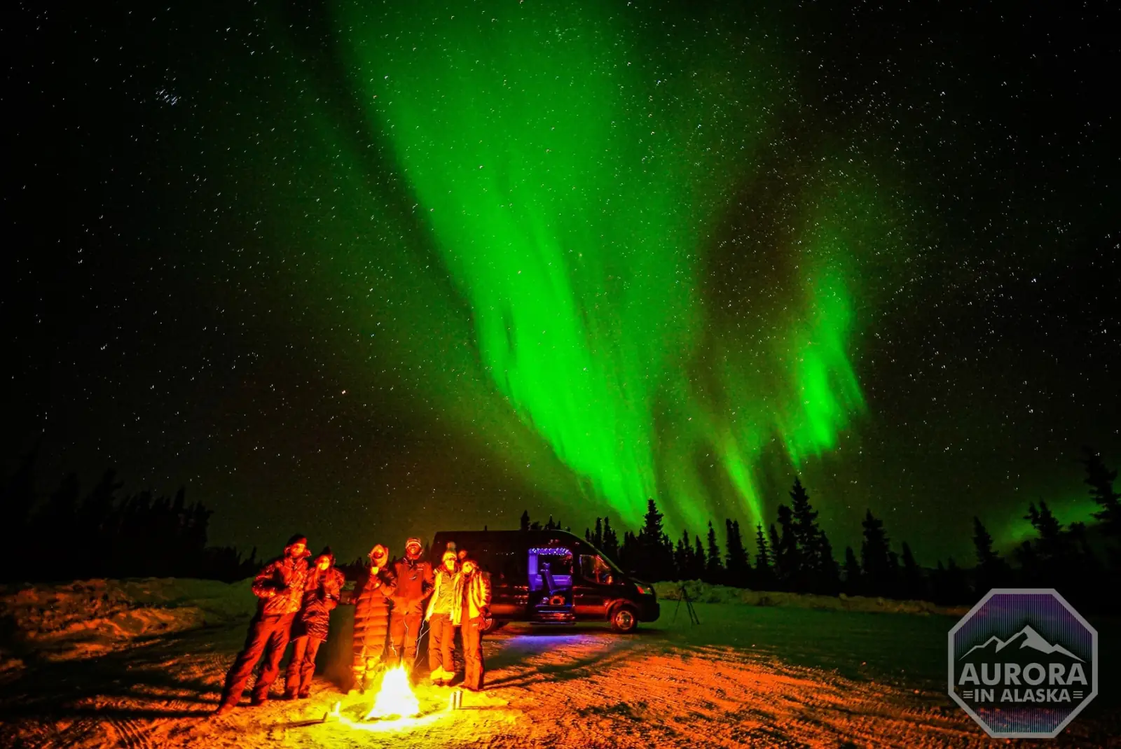 Guests around a campfire under the aurora.