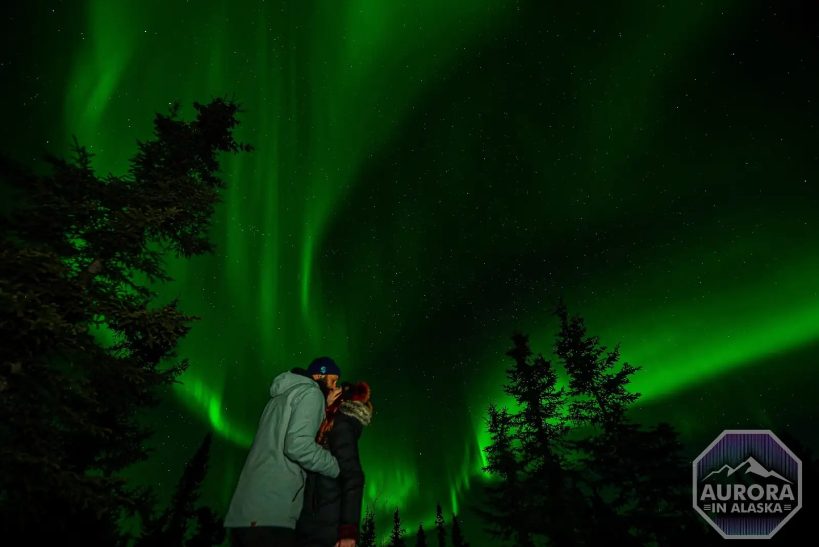 A couple stands together beneath the aurora.