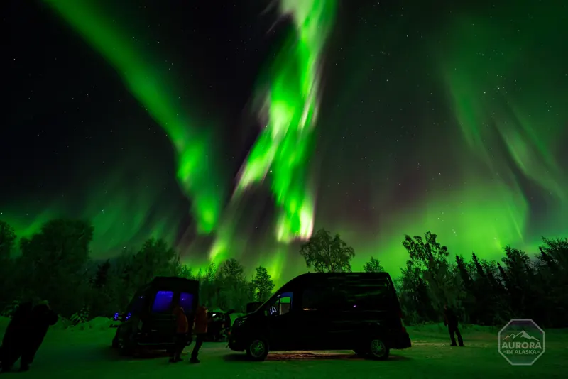 Two black SkyChase Sprinter vans parked under a bright green aurora.
